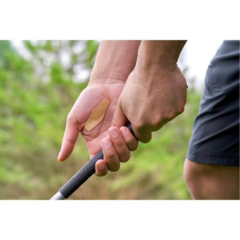 Hand hält Golfschläger, Pflaster auf dem Daumen. Hintergrund: grünes Gras.