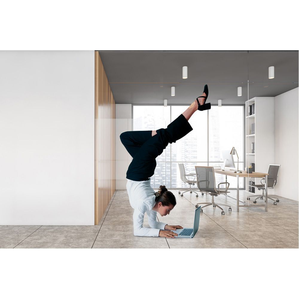 Person macht Handstand am Boden, Laptop vor sich. Hintergrund: Büro mit Fenstern.