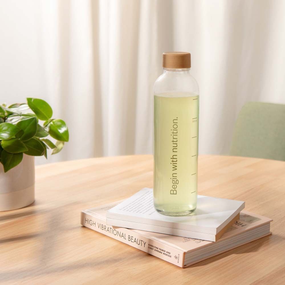 Eine Glasflasche mit Flüssigkeit, beschriftet 'Begin with nutrition'. Auf Büchern auf einem Tisch.