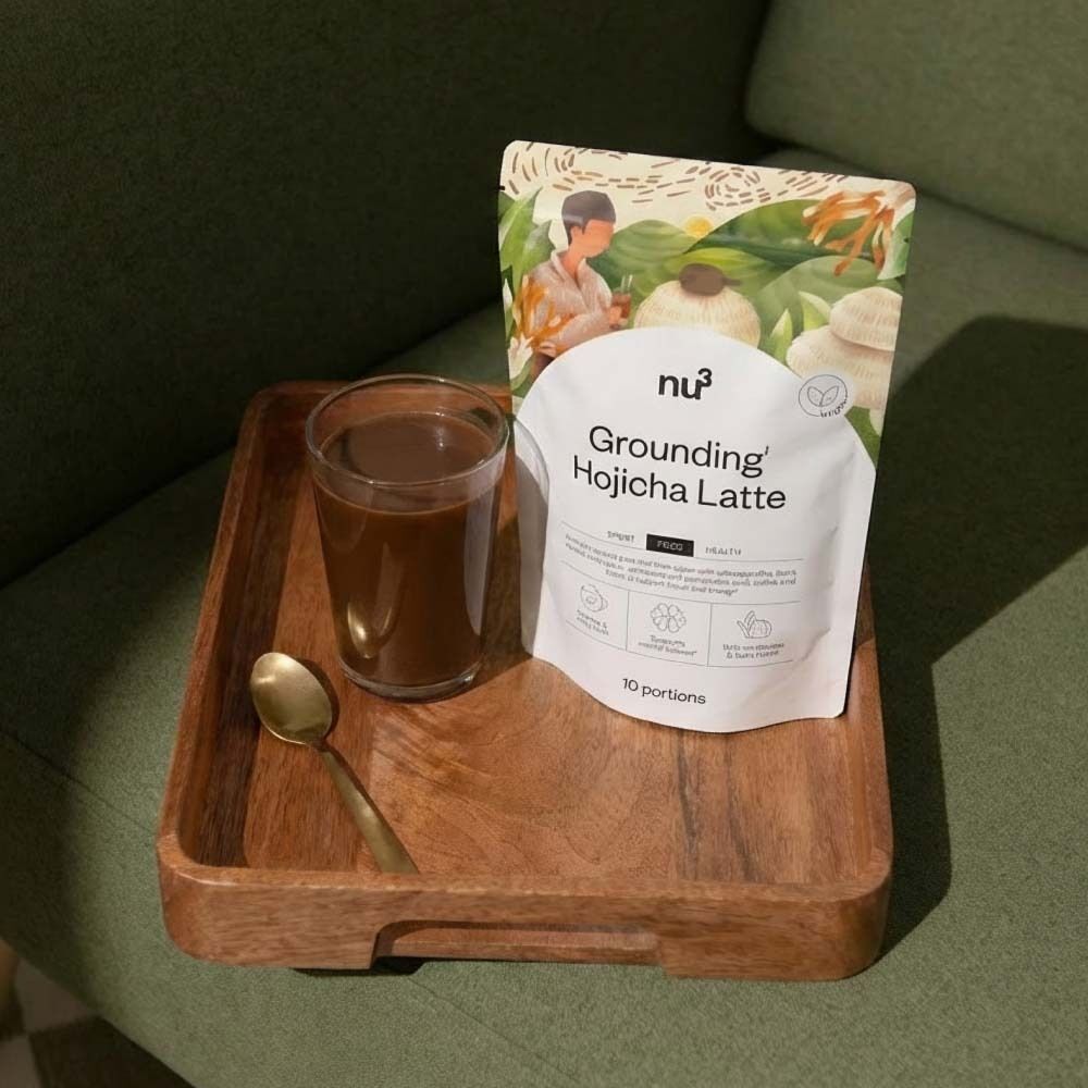 Beutel nu3 Grounding Hojicha Latte, Glas mit Getränk, Löffel auf Holztablett. Produktname und Vegan-Siegel.