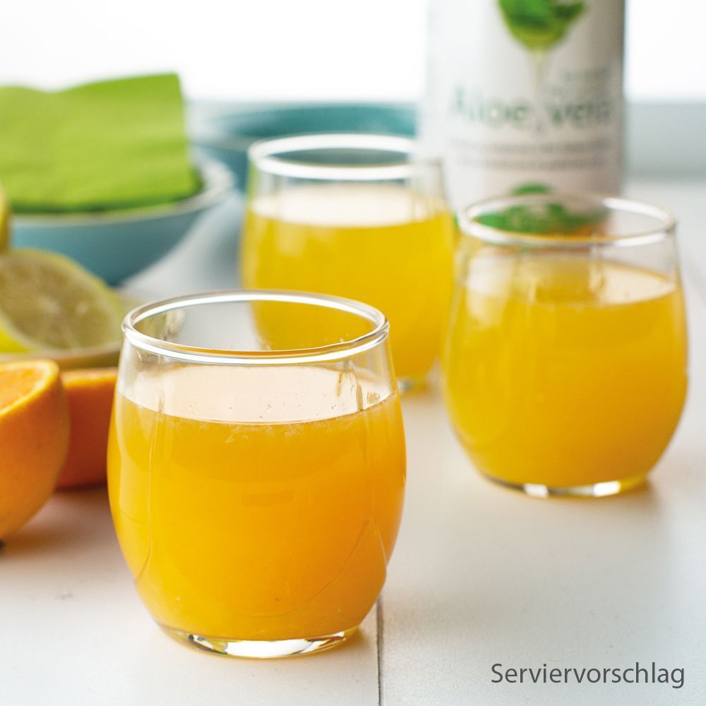 Drei Gläser mit gelbem Saft, wahrscheinlich Aloe Vera Saft, auf einem Tisch mit Orangen- und Zitronenscheiben.