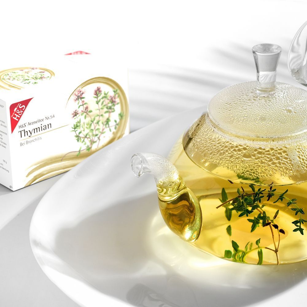 H&S Thymian Nr. 54 Kräutertee Packung neben einer Glaskanne mit aufgebrühtem Thymiantee.