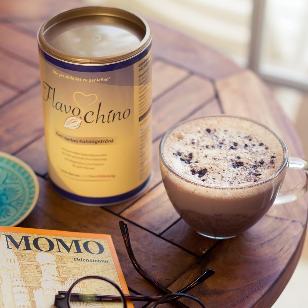 Dose FLAVOCHINO Dr. Jacob's und Glas mit Schokolade. Auf Tisch mit Brille und Buch.