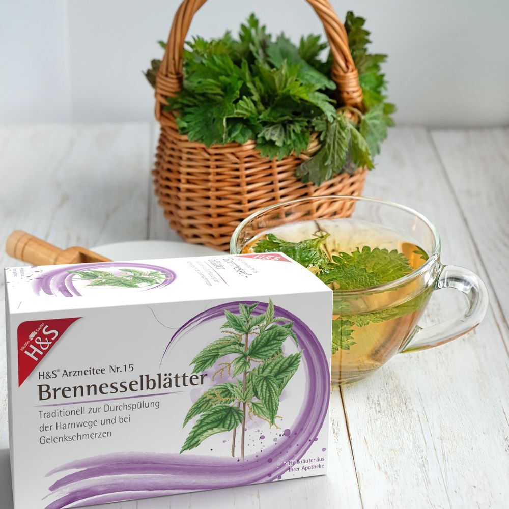 H&S Brennnesselblätter Nr. 15 Tee Packung neben einer Tasse Tee und einem Korb voller Brennnesseln.