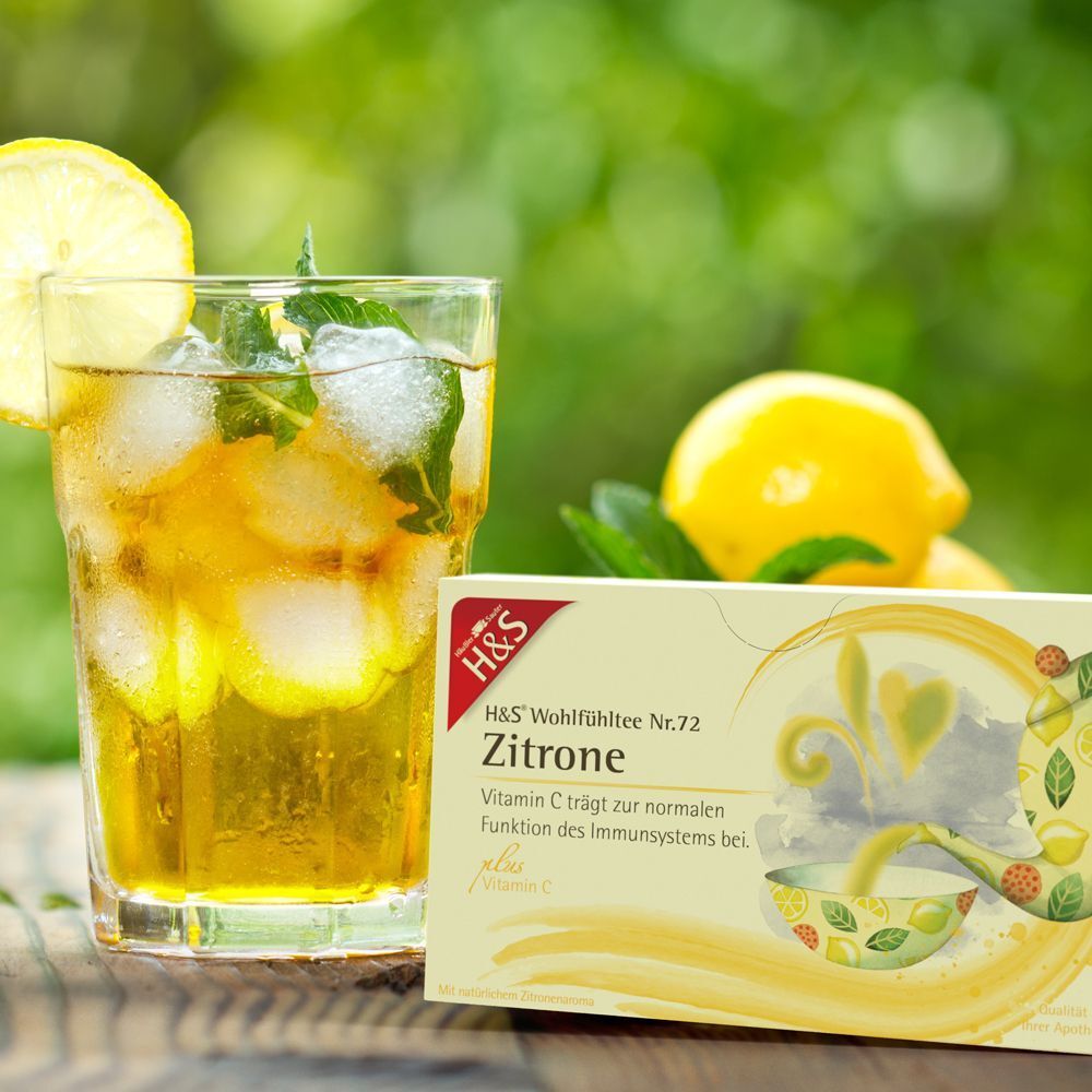 Glas mit Eiswürfeln und gelbem Getränk, Zitrone und H&S Zitrone mit Vitamin C Filterbeutel Packung. Natürlicher Hintergrund.