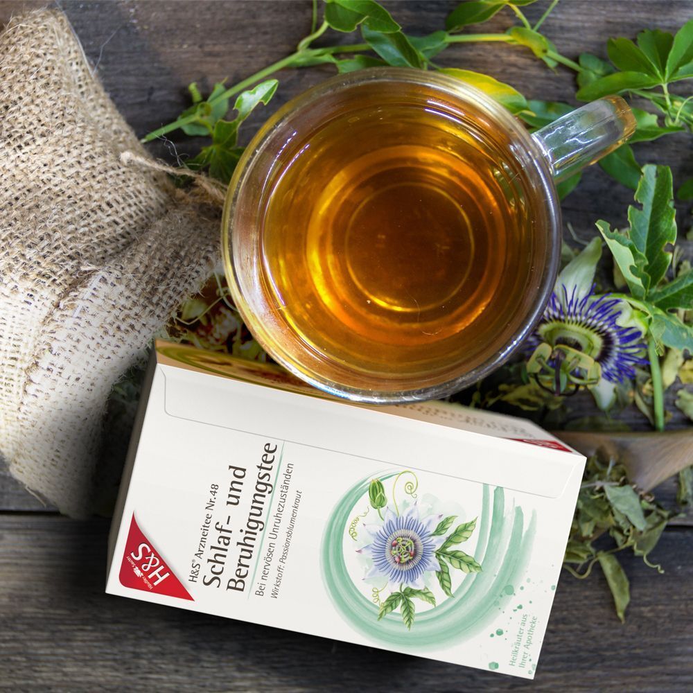 Eine Tasse H&S® Schlaf- und Beruhigungstee neben der Packung und Passionsblumen.