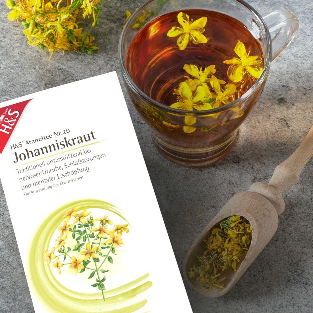 Tasse Johanniskrauttee mit Blüten, Beipackzettel und Holzschaufel mit Kraut.