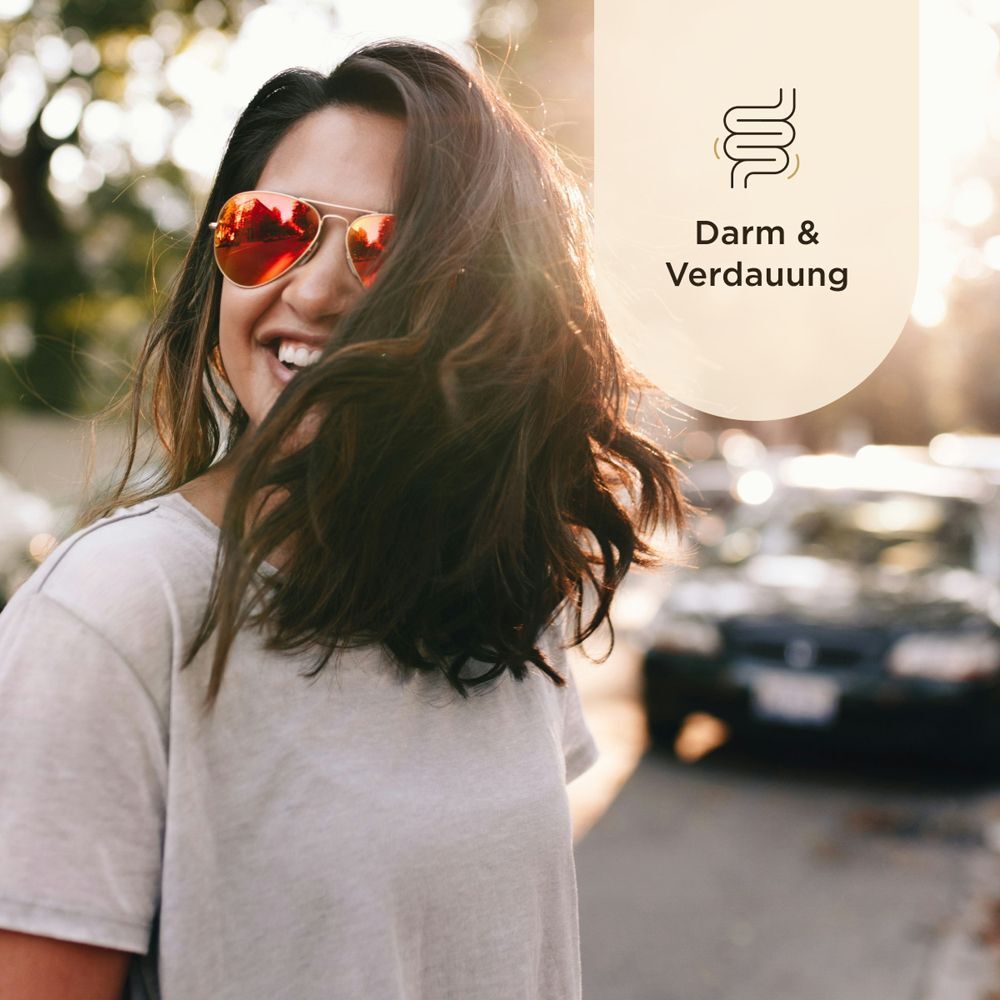 Eine lächelnde Frau mit Sonnenbrille. Hintergrund: verschwommene Straße und ein Symbol für Darm & Verdauung.
