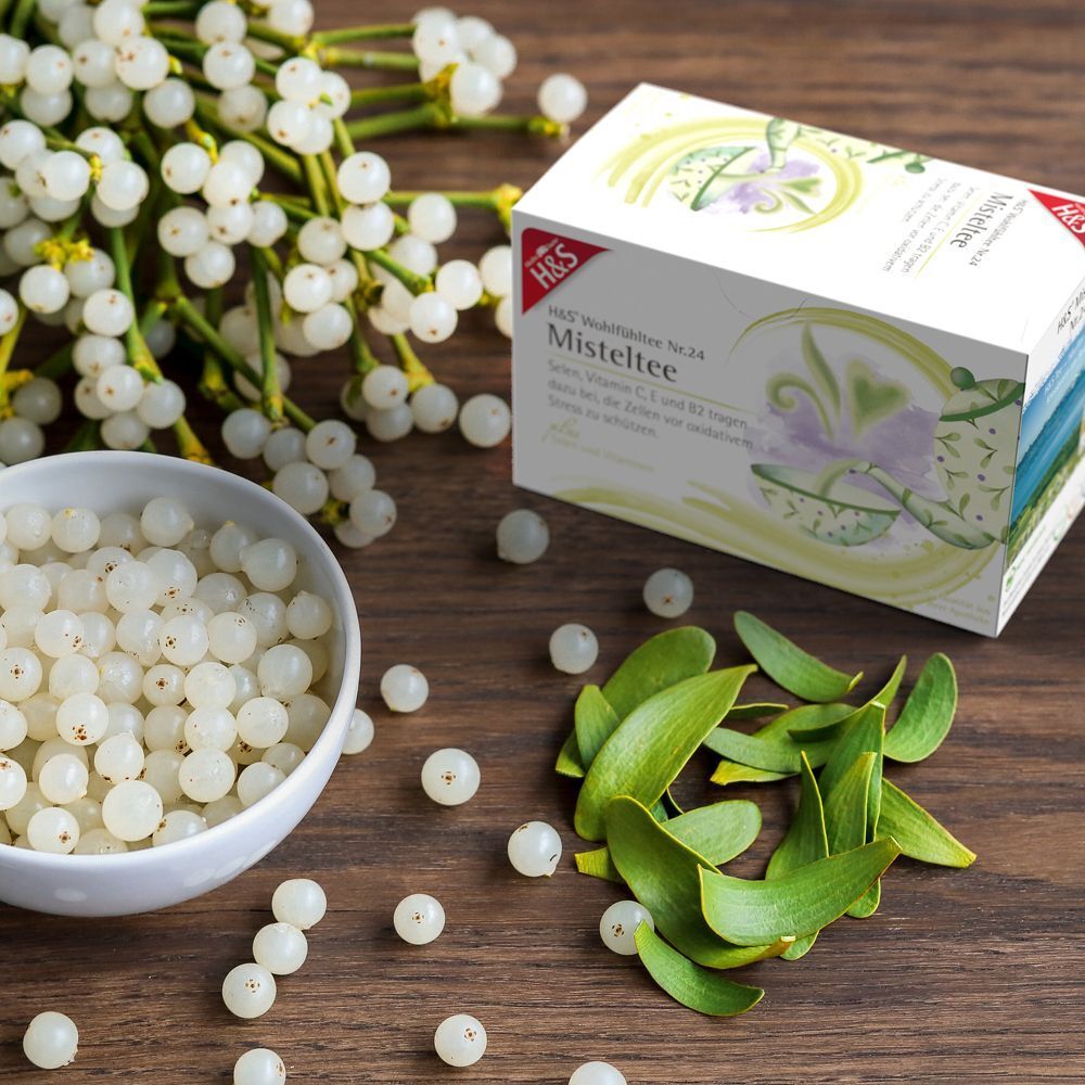 Produktverpackung mit Mistelzweigen, Beeren und einer Schale. Aufdruck: H&S Misteltee. Produkt und Zutaten auf Holzuntergrund.