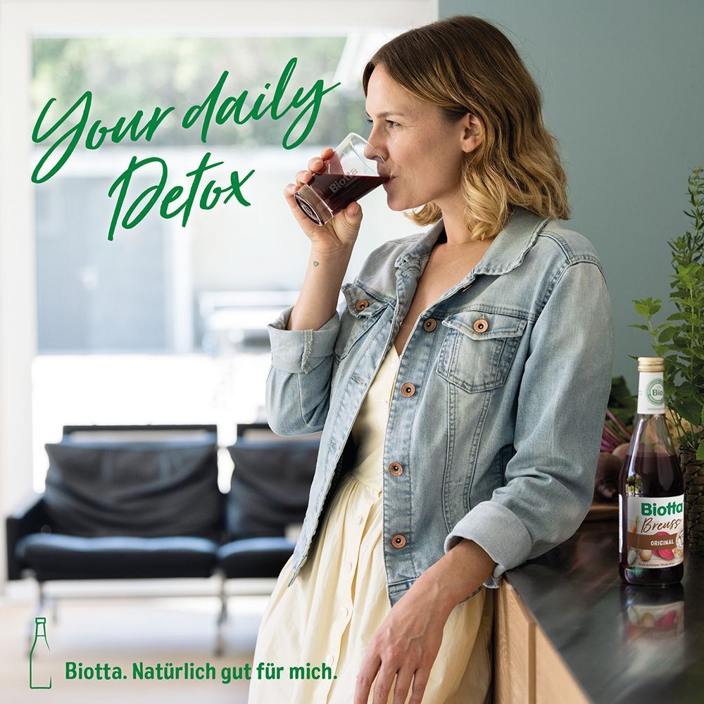 Frau trinkt Biotta® Breuss Antioxidant. Flasche im Hintergrund.