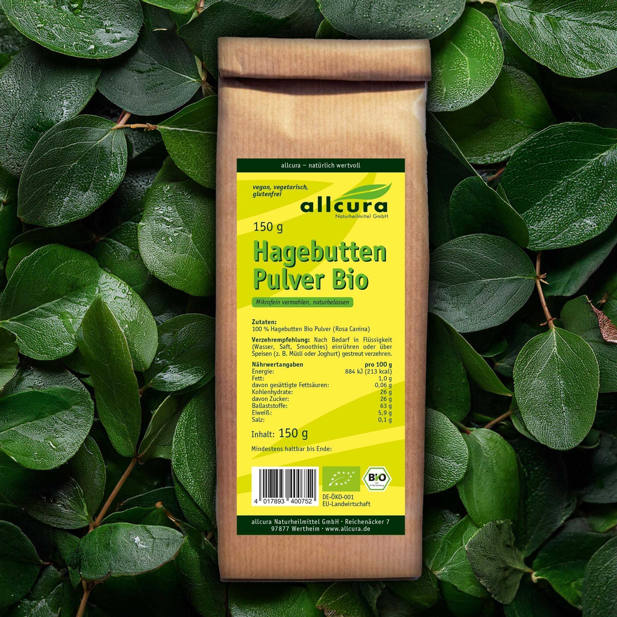 Brauner Papierbeutel mit Etikett, umgeben von grünen Blättern. Aufschrift: allcura, Hagebutten Pulver Bio, 150g. Bio-Siegel.