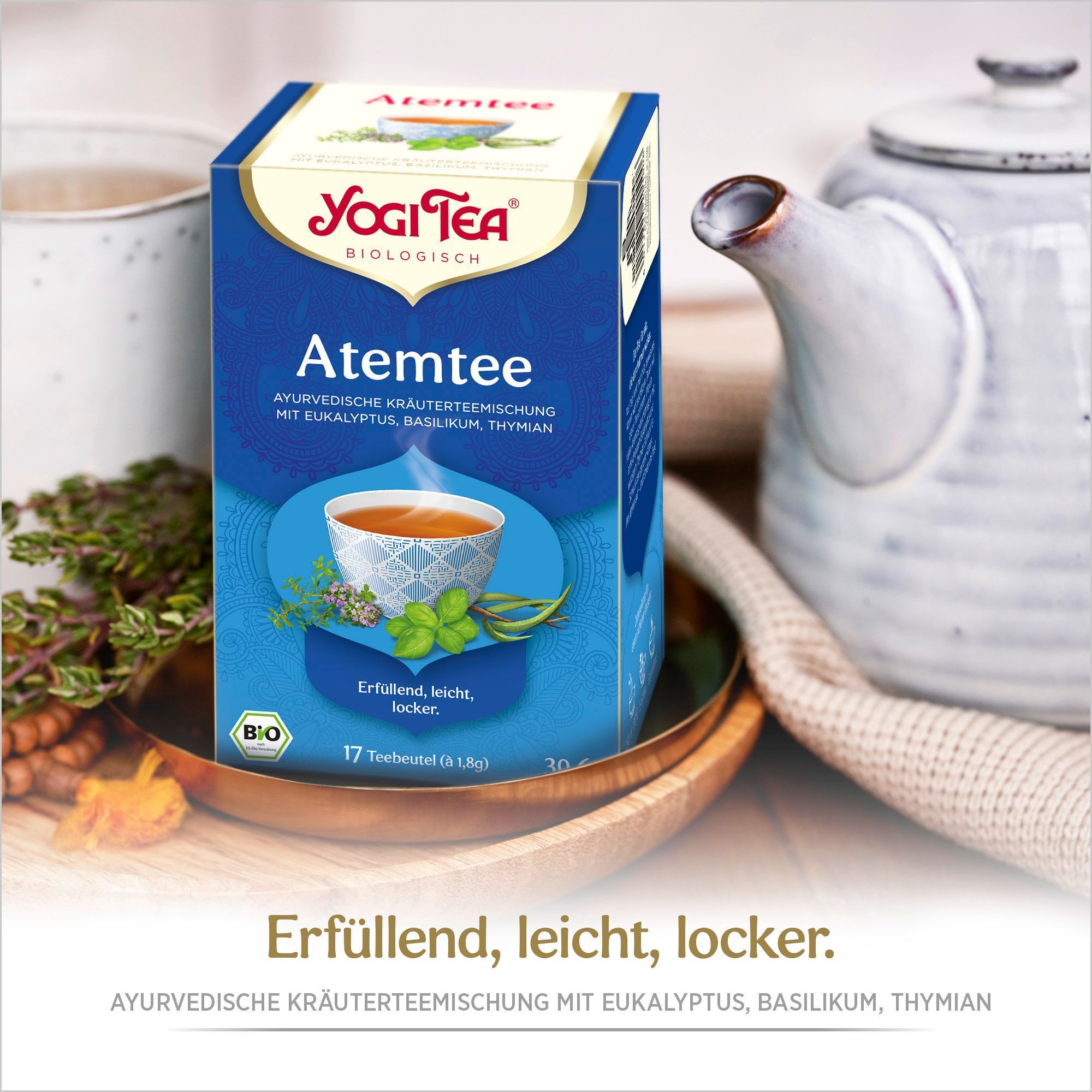 Teepackung auf einem Tablett. Blaue Verpackung mit Logo und Produktnamen. Eine Tasse und eine Kanne im Hintergrund.
