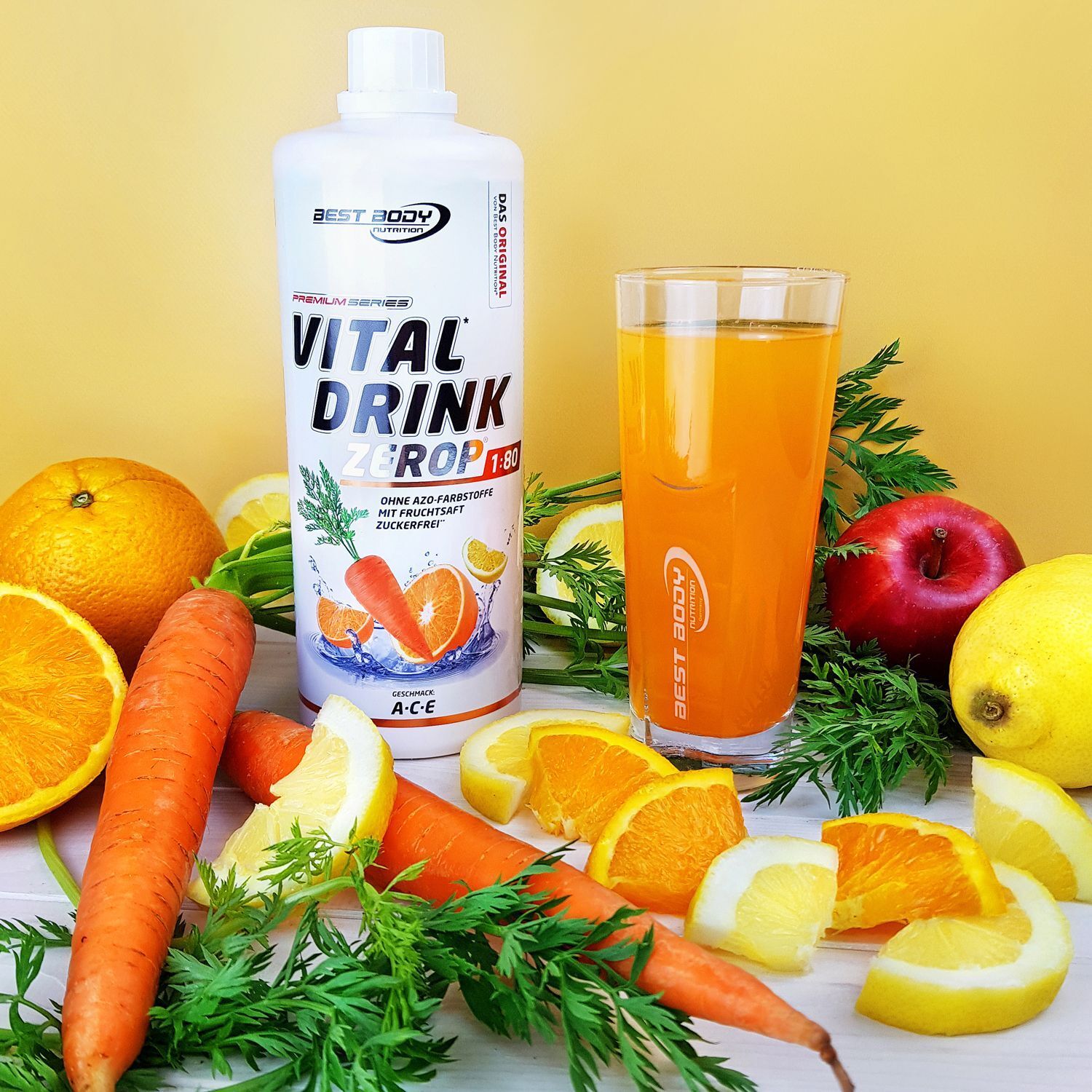 Flasche BBN Vital Drink ZERO neben einem Glas Getränk. Umgeben von Obst und Gemüse, wie Karotten und Zitronen.