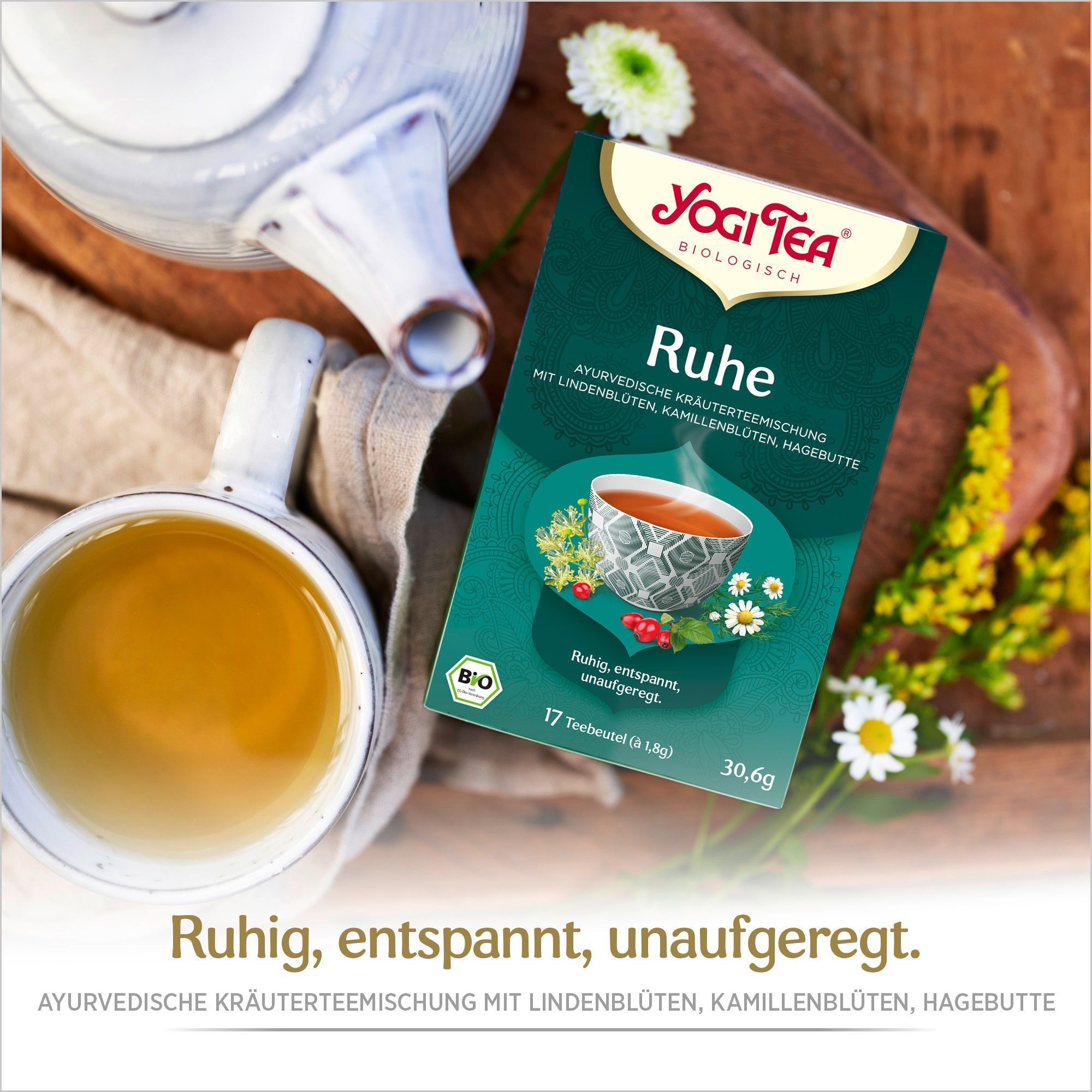 YOGI TEA Ruhe Bio Filterbeutel neben einer Tasse Tee und Teekanne. Aufschrift: Ruhe, ayurvedische Kräutermischung. Mit Bio-Siegel.