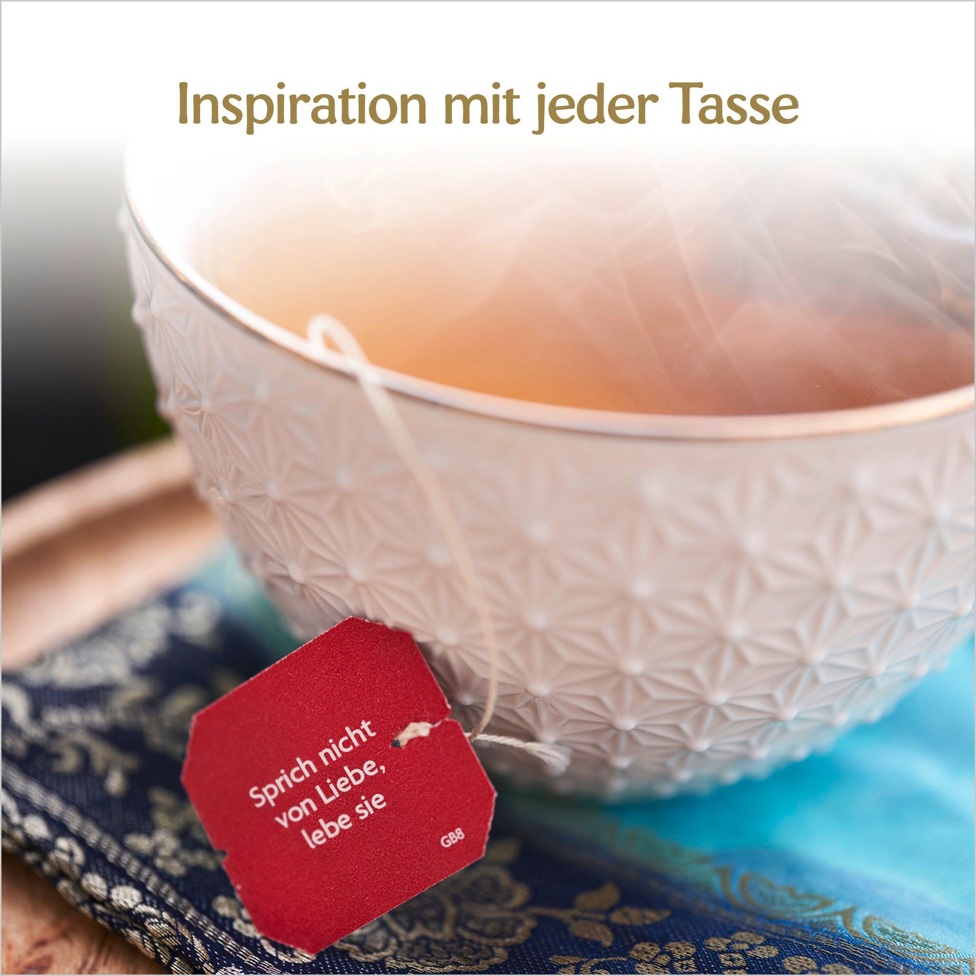 Weiße Tasse mit Teebeutel. Auf dem Teebeutel steht: Sprich nicht von Liebe, lebe sie.