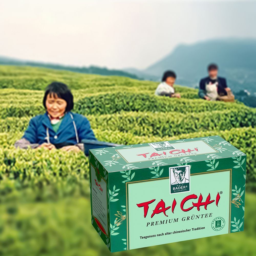 Grüner Karton mit "TAI CHI Premium Grüntee"-Logo, vor einer Szene mit Teepflückern. Produktverpackung im Feld.
