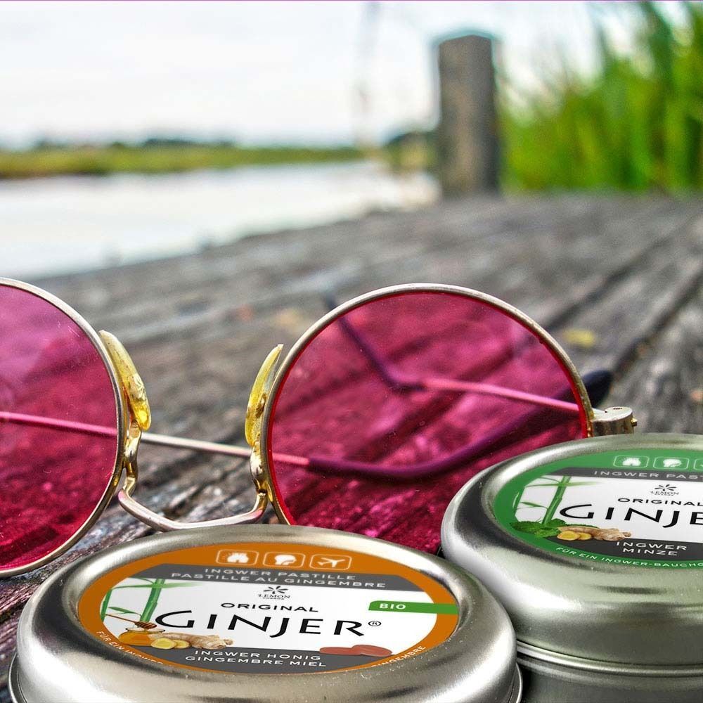 Drei runde Metalldosen mit Etiketten. Aufschrift: GINJER Pastille, Ingwer Honig. Bio-Siegel. Sonnenbrille.