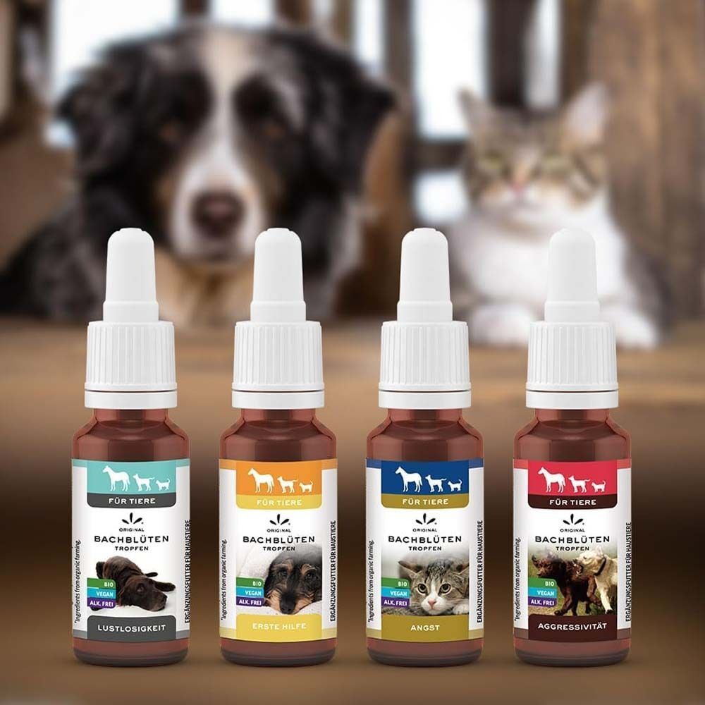 Vier Flaschen mit Tropfen, Etiketten mit Produktnamen und Tierabbildungen. Im Hintergrund Hund und Katze unscharf.