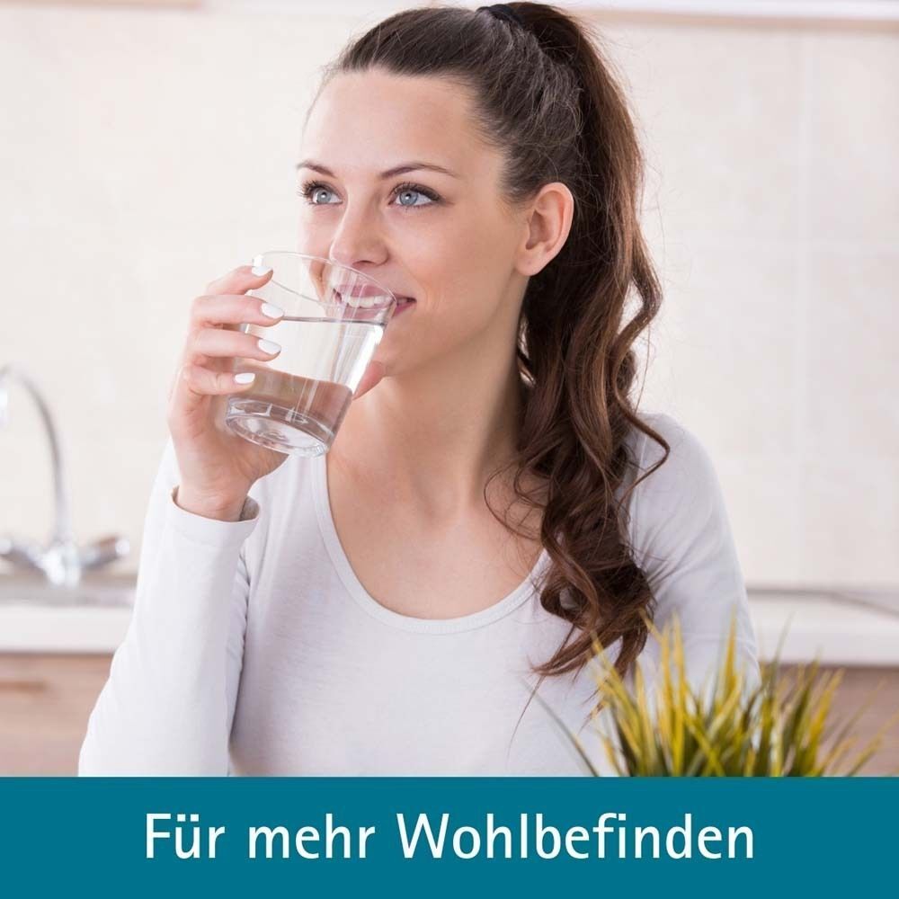 Frau trinkt ein Glas Wasser in einer hellen Küche.