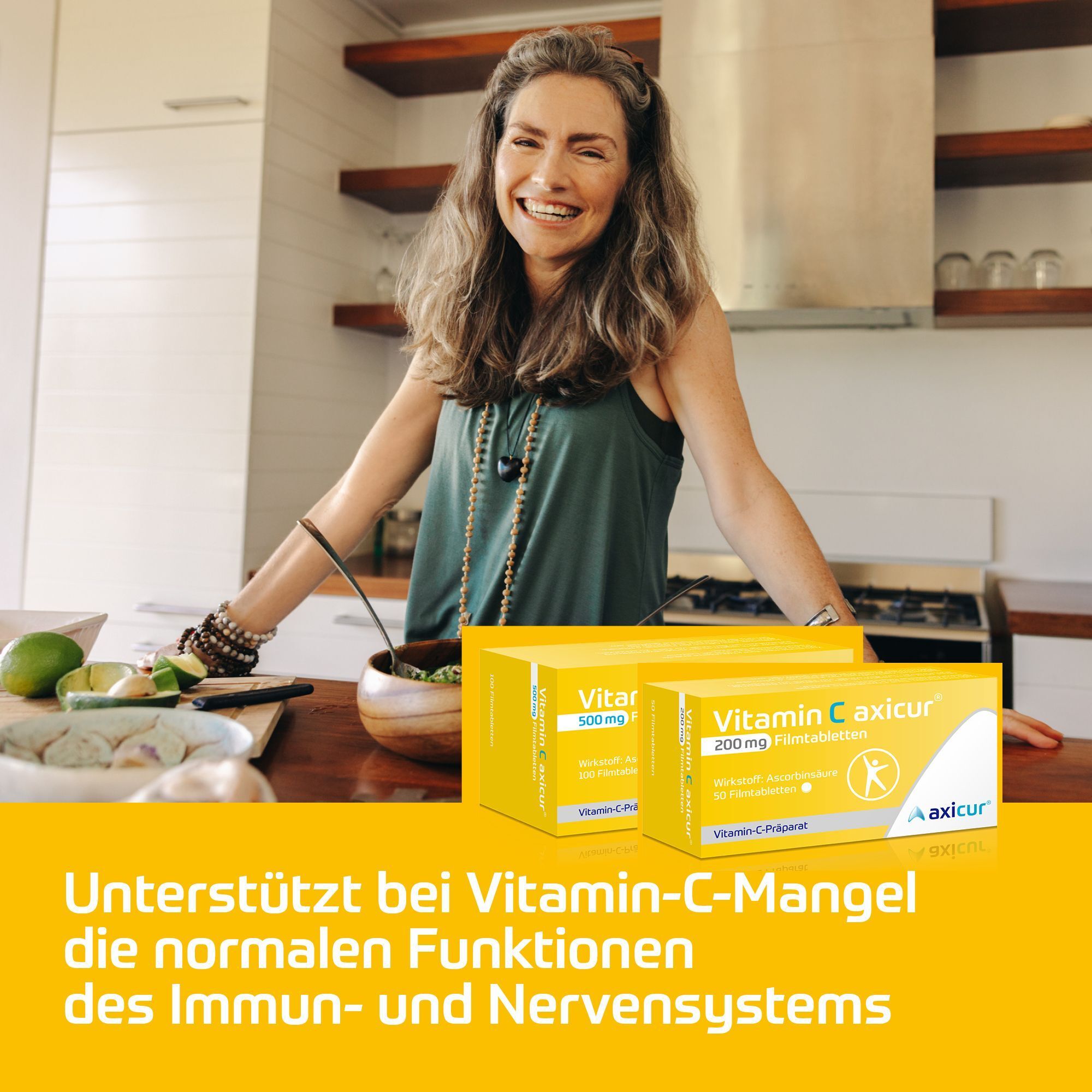 Packungen Vitamin C axicur® in einer Küche, mit einer lächelnden Frau im Hintergrund.