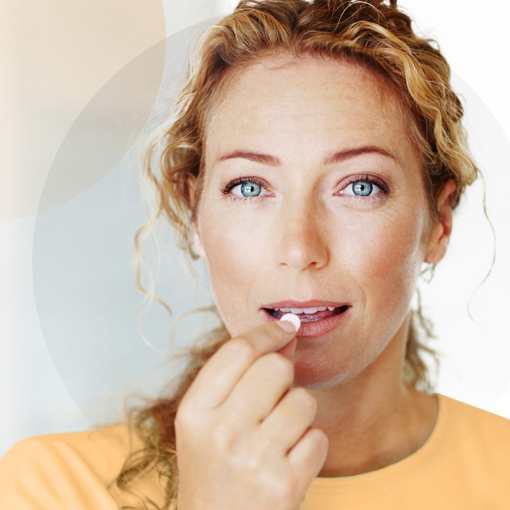 Frau mit blauen Augen nimmt eine weiße Tablette ein.