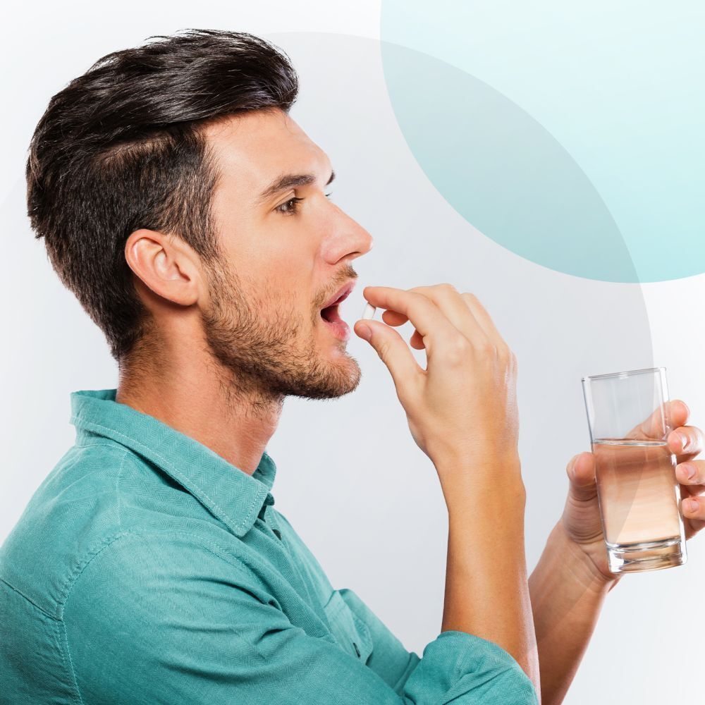 Mann nimmt eine weiße Hartkapsel ein und hält ein Glas Wasser.