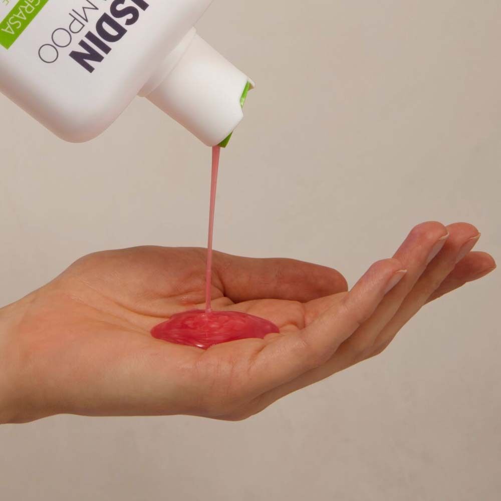 Rosa Shampoo wird aus einer ISDIN Nutradeica Flasche in eine Handfläche gegossen.