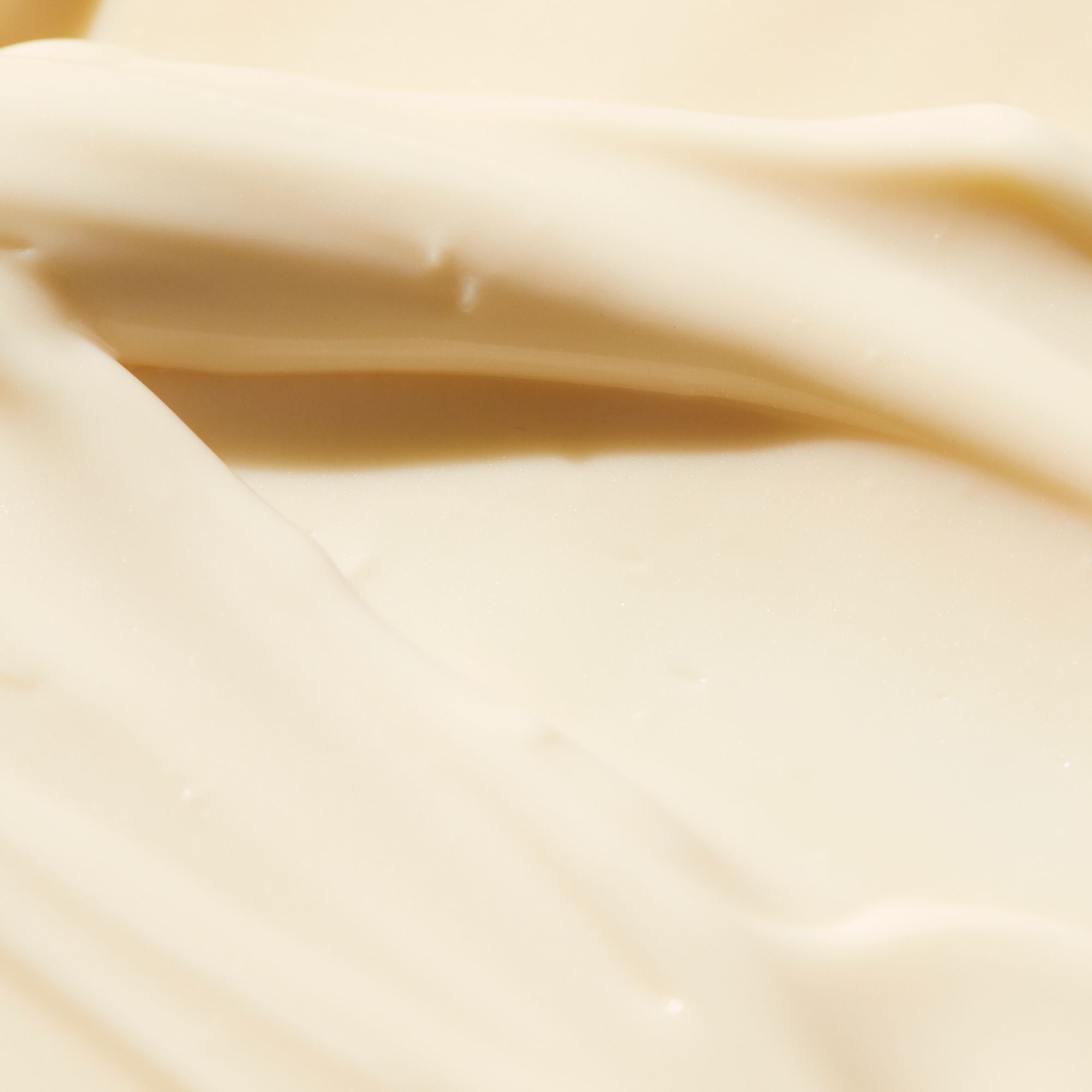 Cremige Textur der NUXE Sun After-Sun-Milch. Helle, gelbliche Lotion in Wellenform.
