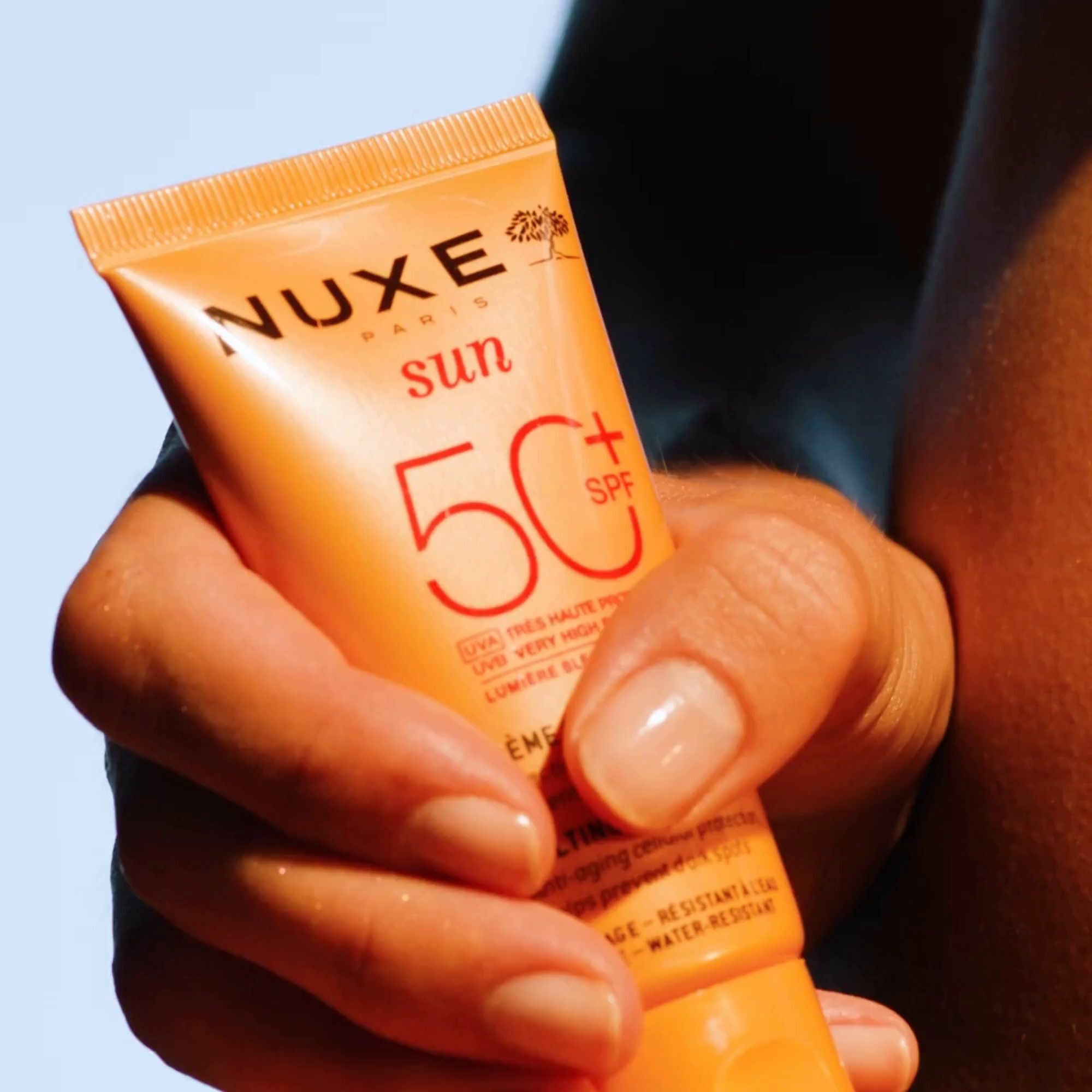 Hand hält Nuxe Sun Sonnencreme Gesicht LSF 50, 50ml.