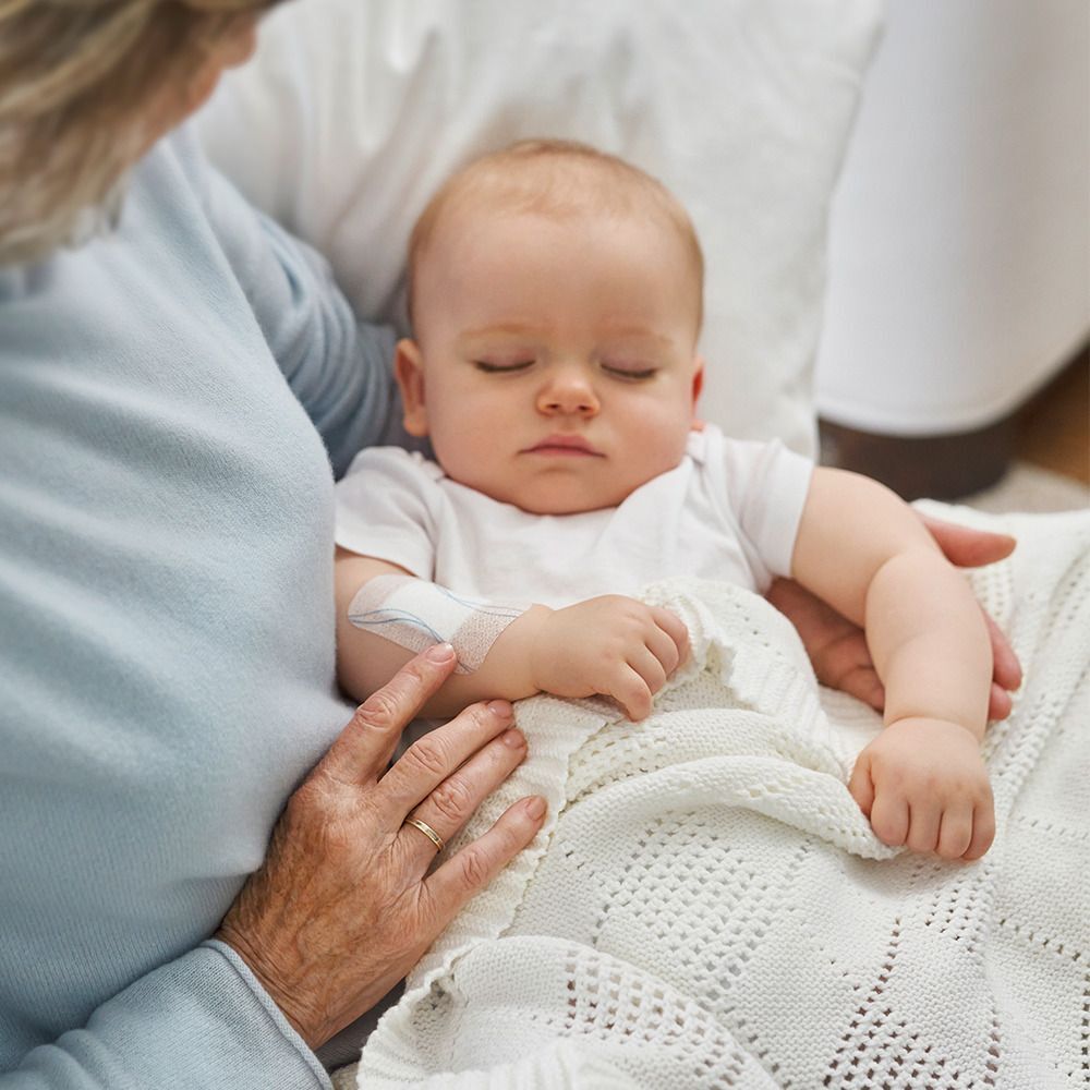 Baby mit einem Verband am Arm, gehalten von einer älteren Person.