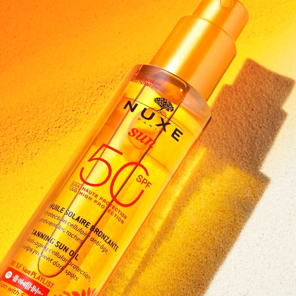 Flasche Nuxe Sun Sonnenöl LSF 50 mit goldgelber Flüssigkeit und orangefarbenem Pumpspray, im Sonnenlicht.