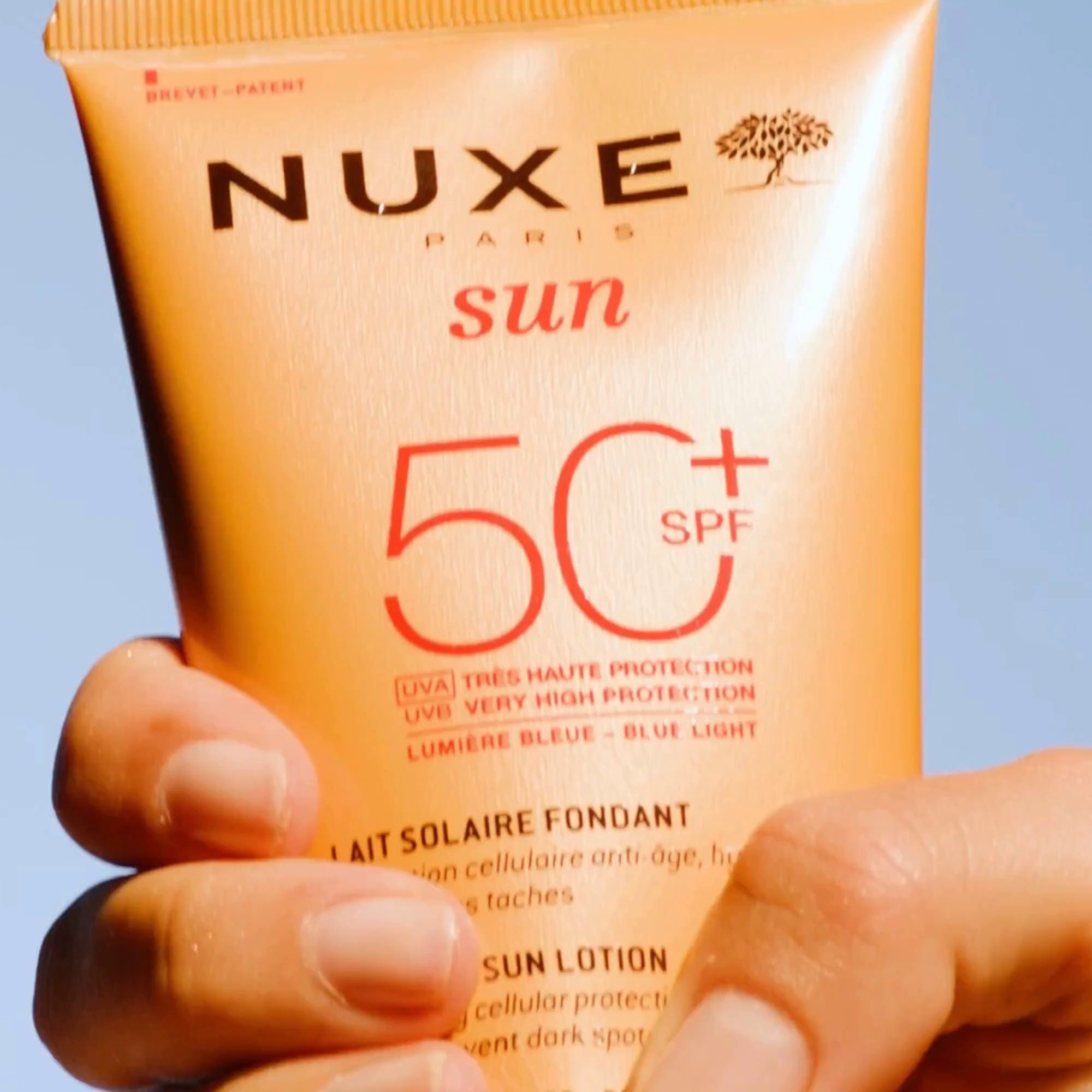 Nahaufnahme einer Hand, die eine Tube NUXE Sun Sonnenmilch LSF 50 hält.