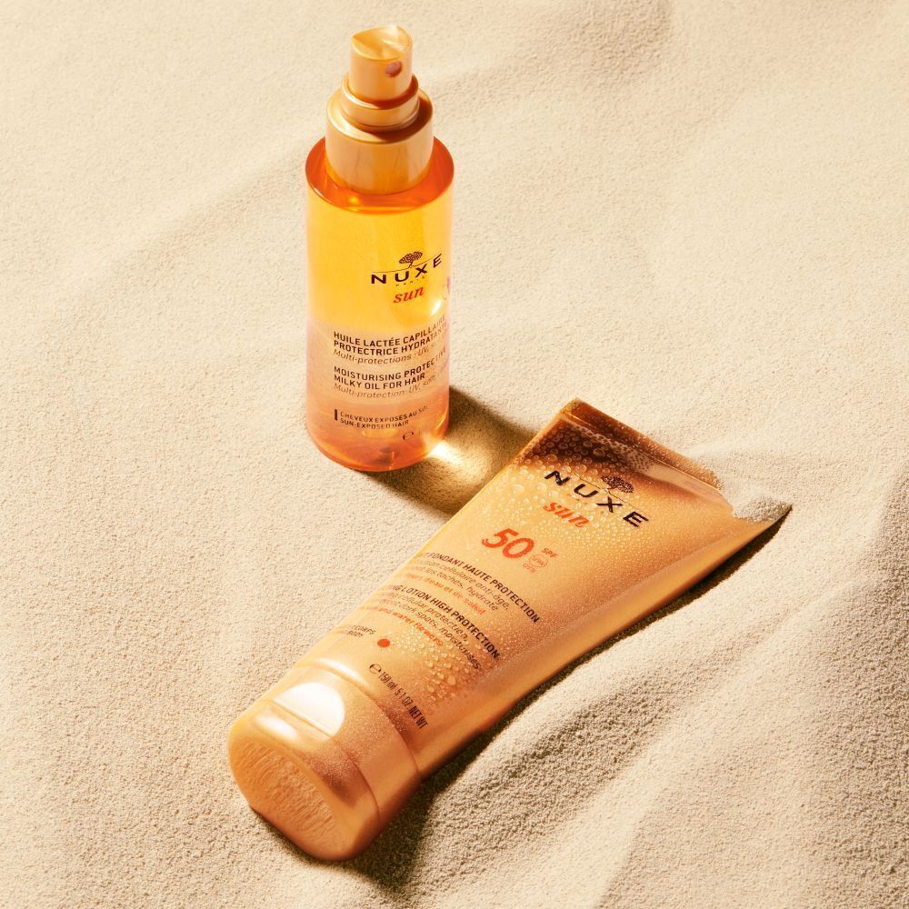 Tube NUXE Sun Sonnenmilch LSF 50 und eine Sprühflasche auf Sand.