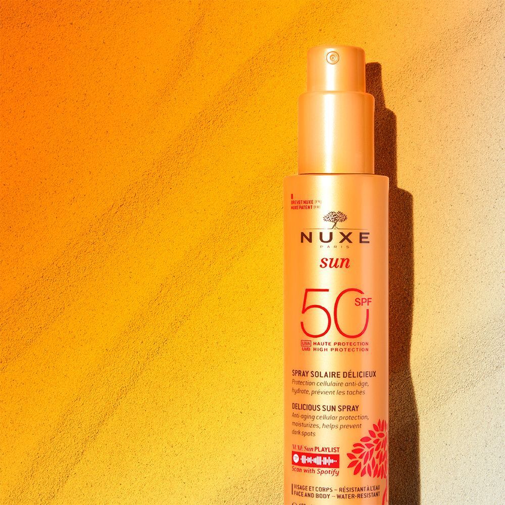 Nuxe Sun Sonnenspray LSF 50 mit Zerstäuber auf sandigem Untergrund.