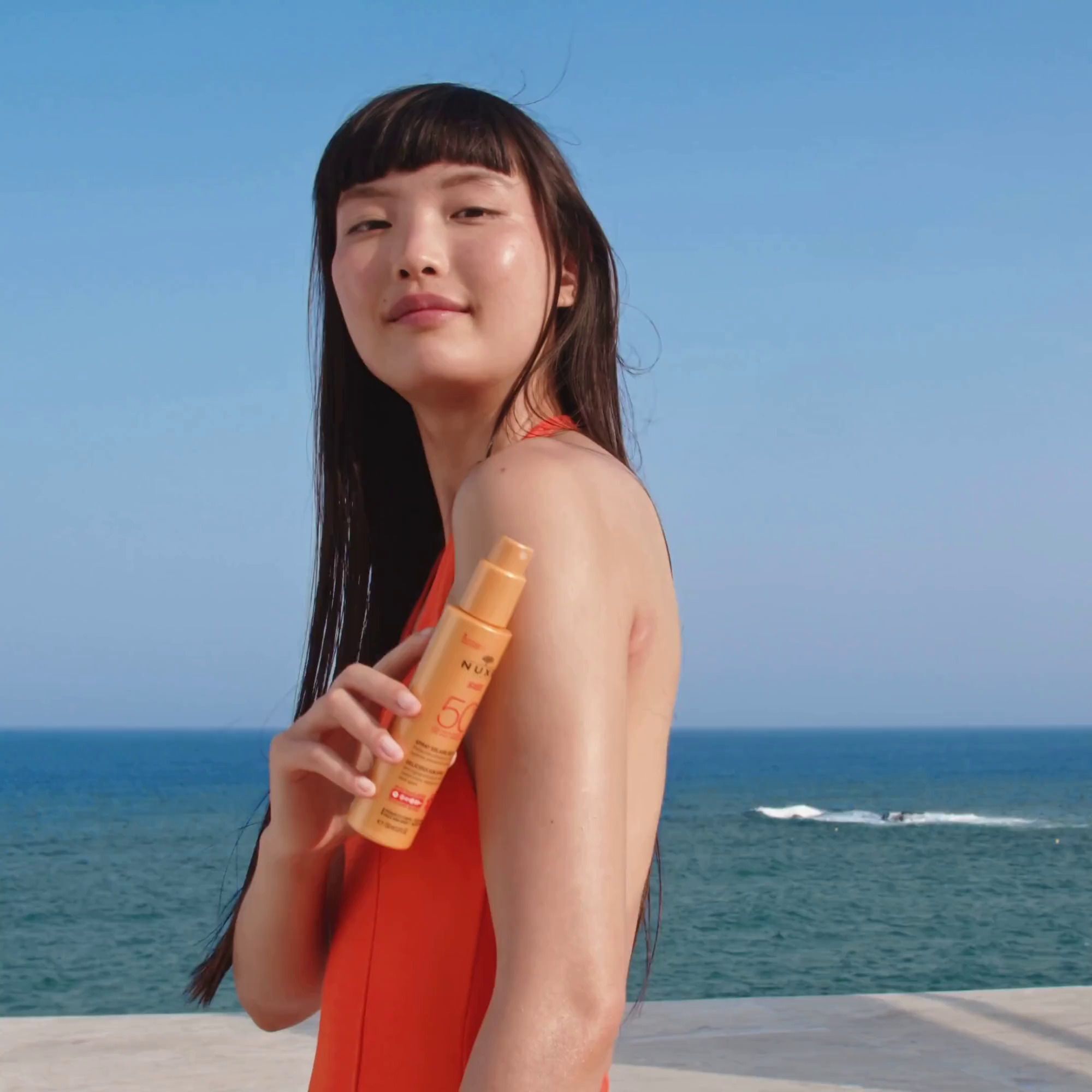 Frau mit NUXE Sonnenspray LSF 50 am Strand.