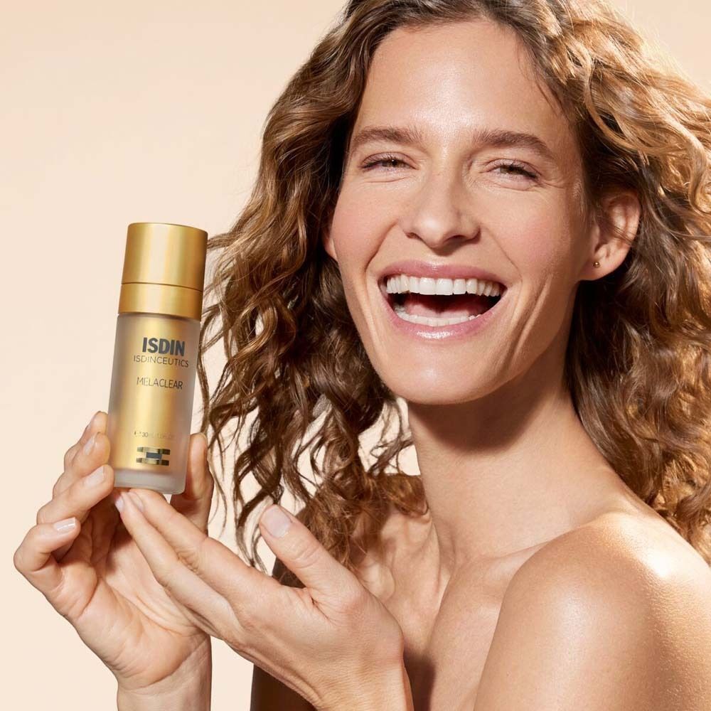 Lächelnde Frau hält eine goldene Flasche ISDIN ISDINCEUTICS Melaclear Serum.