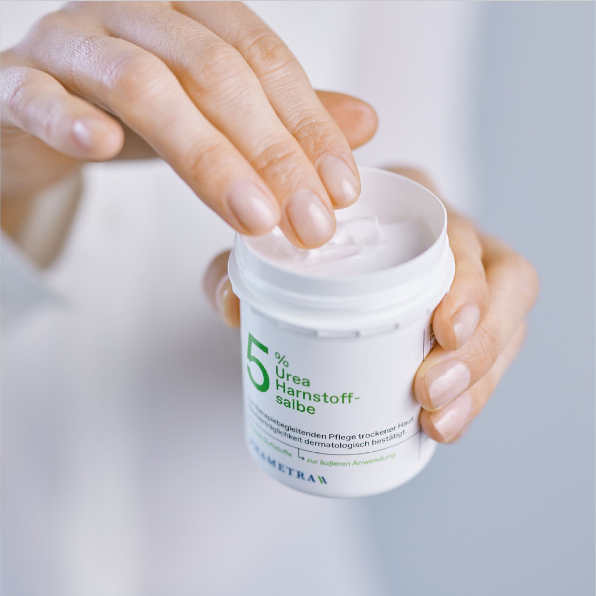Eine Hand öffnet einen Tiegel mit 5% Urea Harnstoffsalbe.