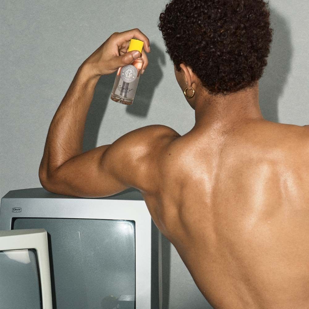 Mann hält ROGER&GALLET Cologne Twist Eau de Cologne Flasche neben einem Fernseher.