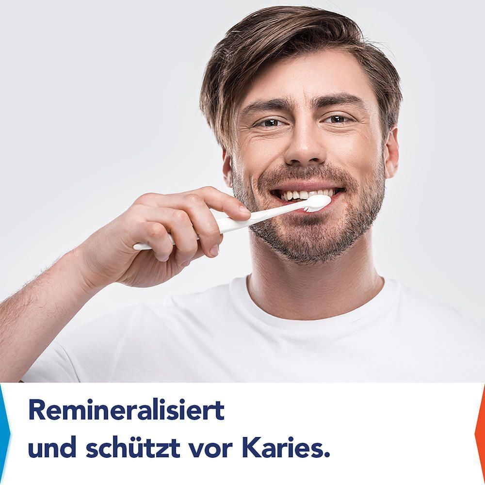 Mann putzt sich lächelnd die Zähne mit einer Zahnbürste, Text: Remineralisiert und schützt vor Karies.