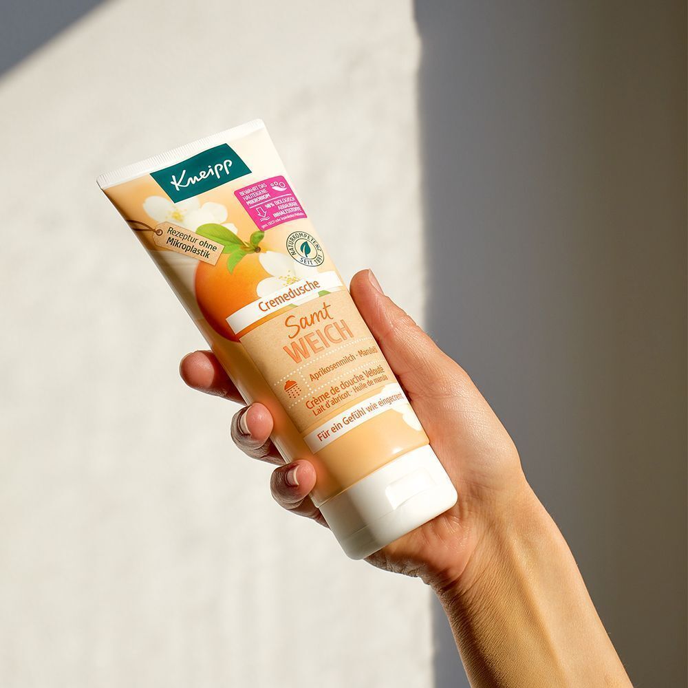 Hand hält eine Tube Kneipp® Cremedusche Samtweich mit Aprikosenmilch und Marulaöl.