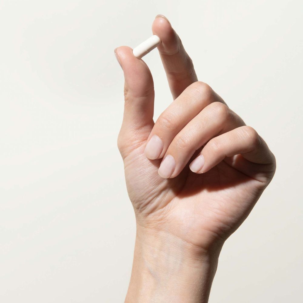 Eine Hand hält eine weiße Kapsel zwischen Daumen und Zeigefinger.