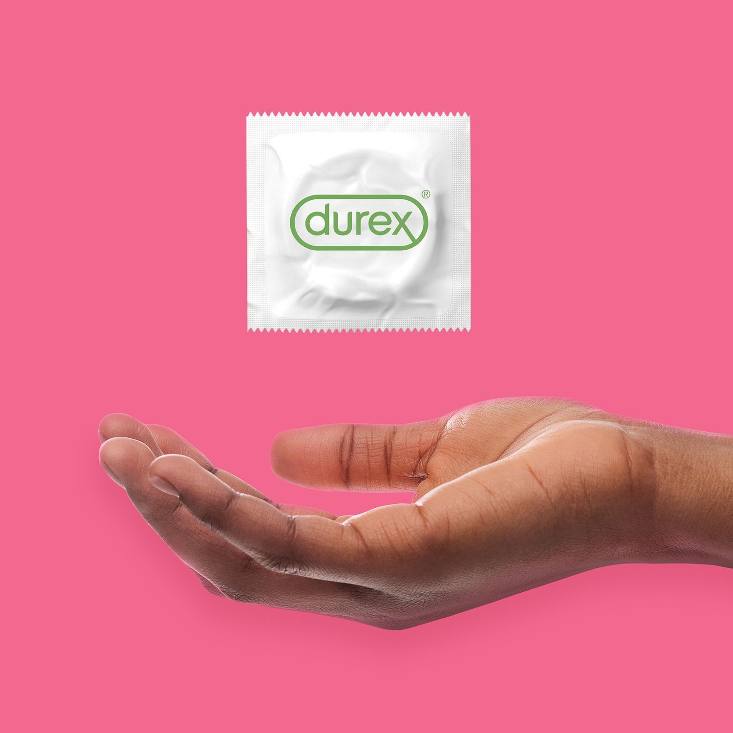 Eine Hand hält ein einzeln verpacktes Durex Kondom über einem pinken Hintergrund.
