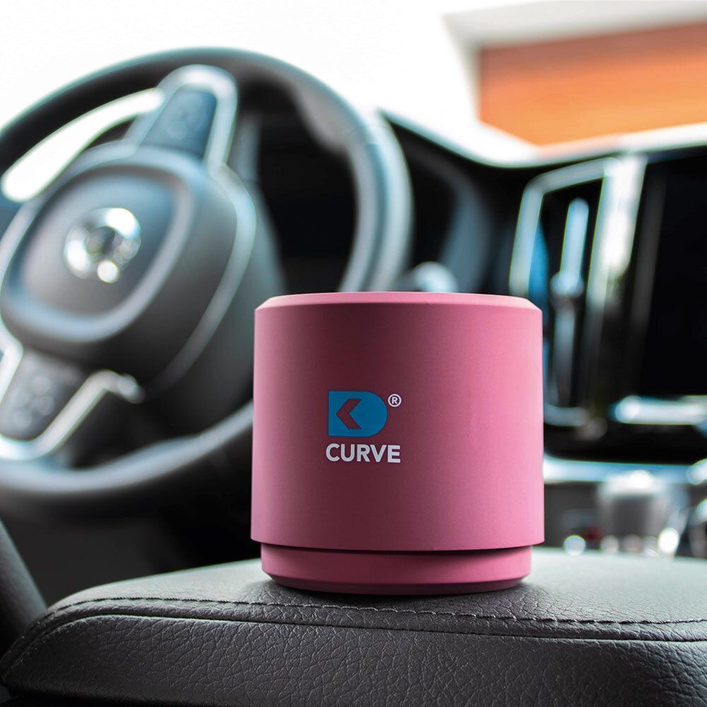 Runder, pinker CURVE Luftreiniger mit blauem Logo auf dem Armaturenbrett eines Autos.