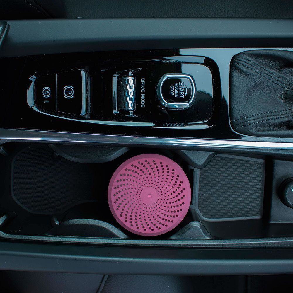 Ein runder, pinker CURVE Luftreiniger in einem Auto-Getränkehalter.