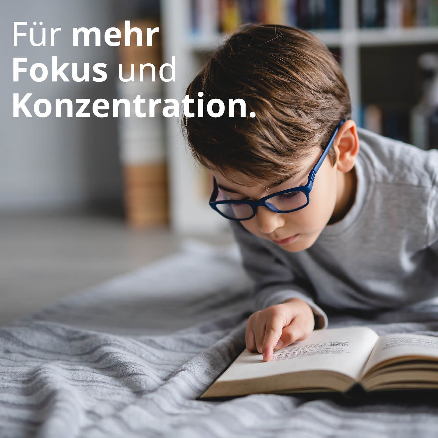 Ein Junge mit Brille liest konzentriert ein Buch auf einer Decke.