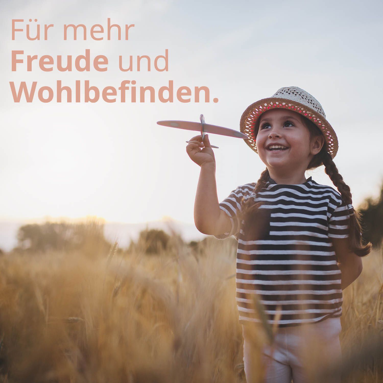 Ein lächelndes Mädchen mit Strohhut spielt mit einem Spielzeugflugzeug im Sonnenuntergang.