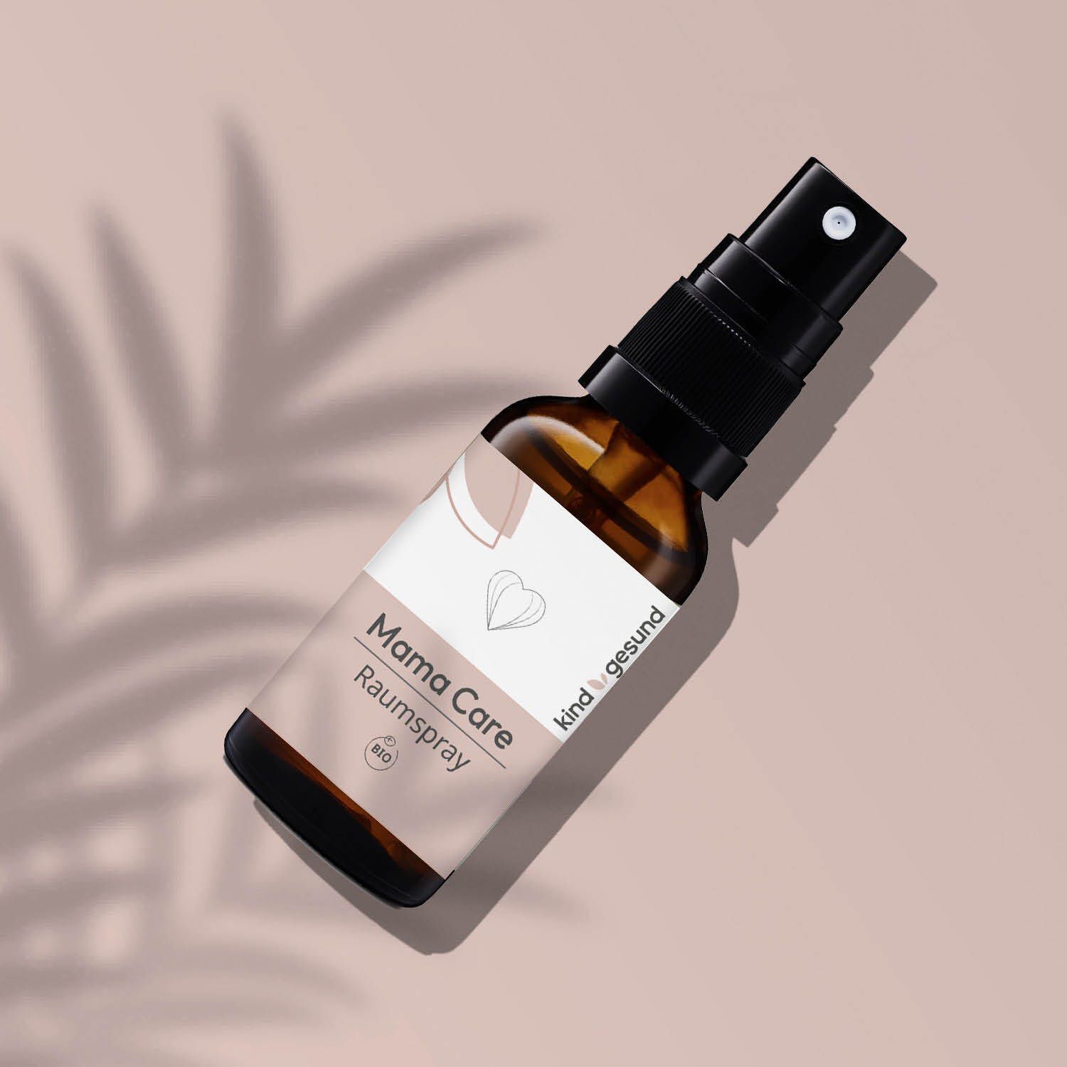 Braune Glasflasche mit Sprayaufsatz, Etikett 'Mama Care Raumsspray', auf rosa Untergrund.