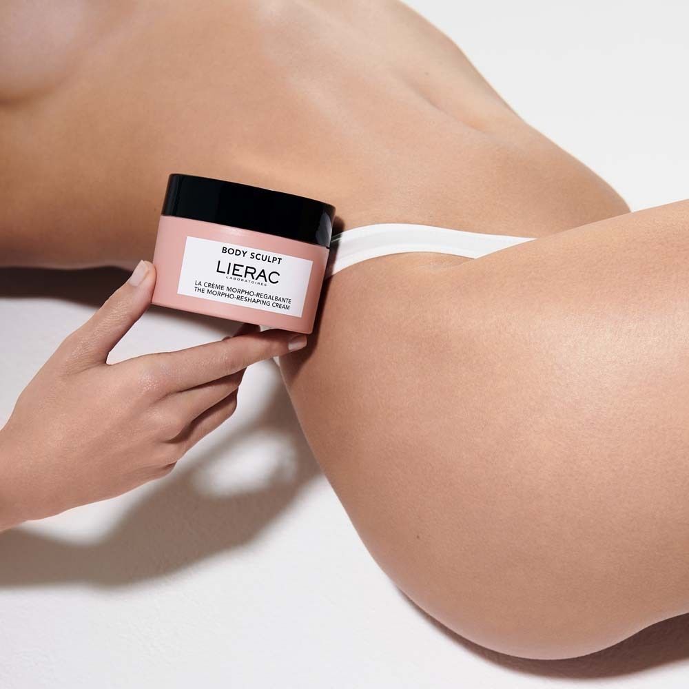 Eine Hand hält einen LIERAC Body Sculpt Körpercreme-Tiegel auf der Haut einer Person.