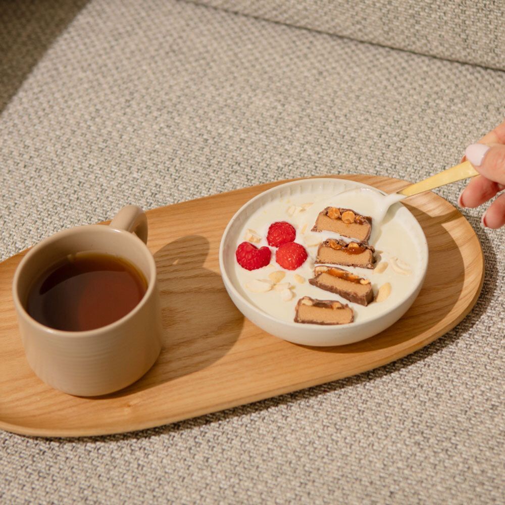 Geschnittene nu3 Fit Protein Riegel in einer Schüssel mit Joghurt, Beeren und Mandelsplittern, daneben eine Tasse Tee.