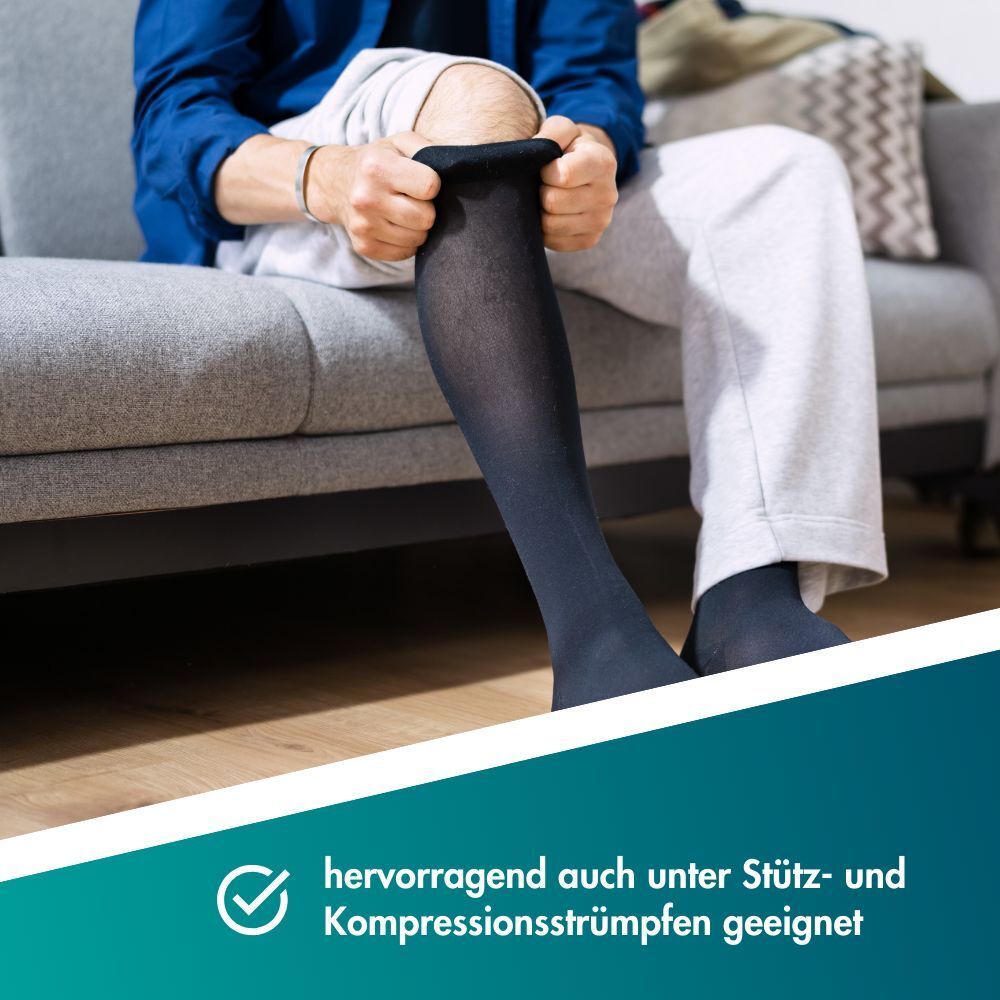 Person zieht Kompressionsstrümpfe an, sitzend auf einem Sofa.